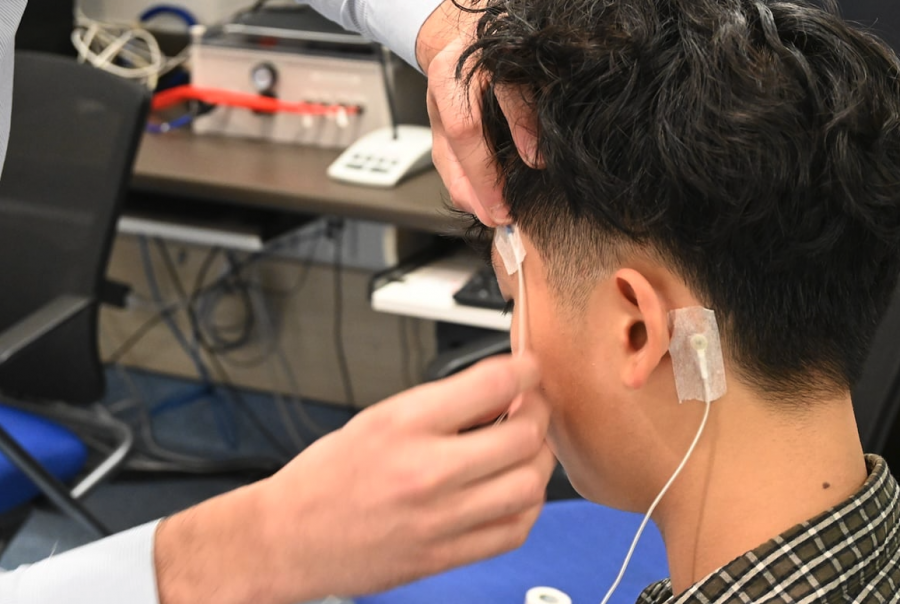 <who> Photo credit: The Tyee/LJI </who> The MEG can pick up electromagnetic signals generated in the brain while a patient takes a nap. If they wear electrodes that track movement, like the ones being attached to this lab assistant’s head, researchers can use an algorithm to clean up the data if a patient moves in their sleep.